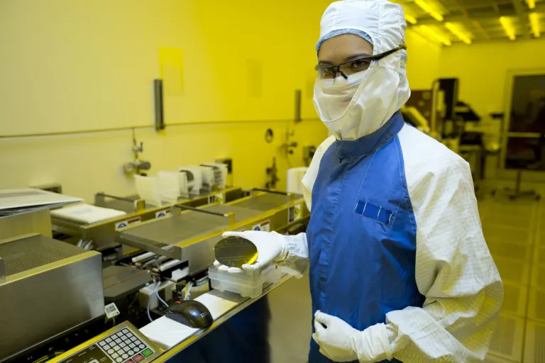 A researcher holds a silicon wafer in a semiconductor cleanroom